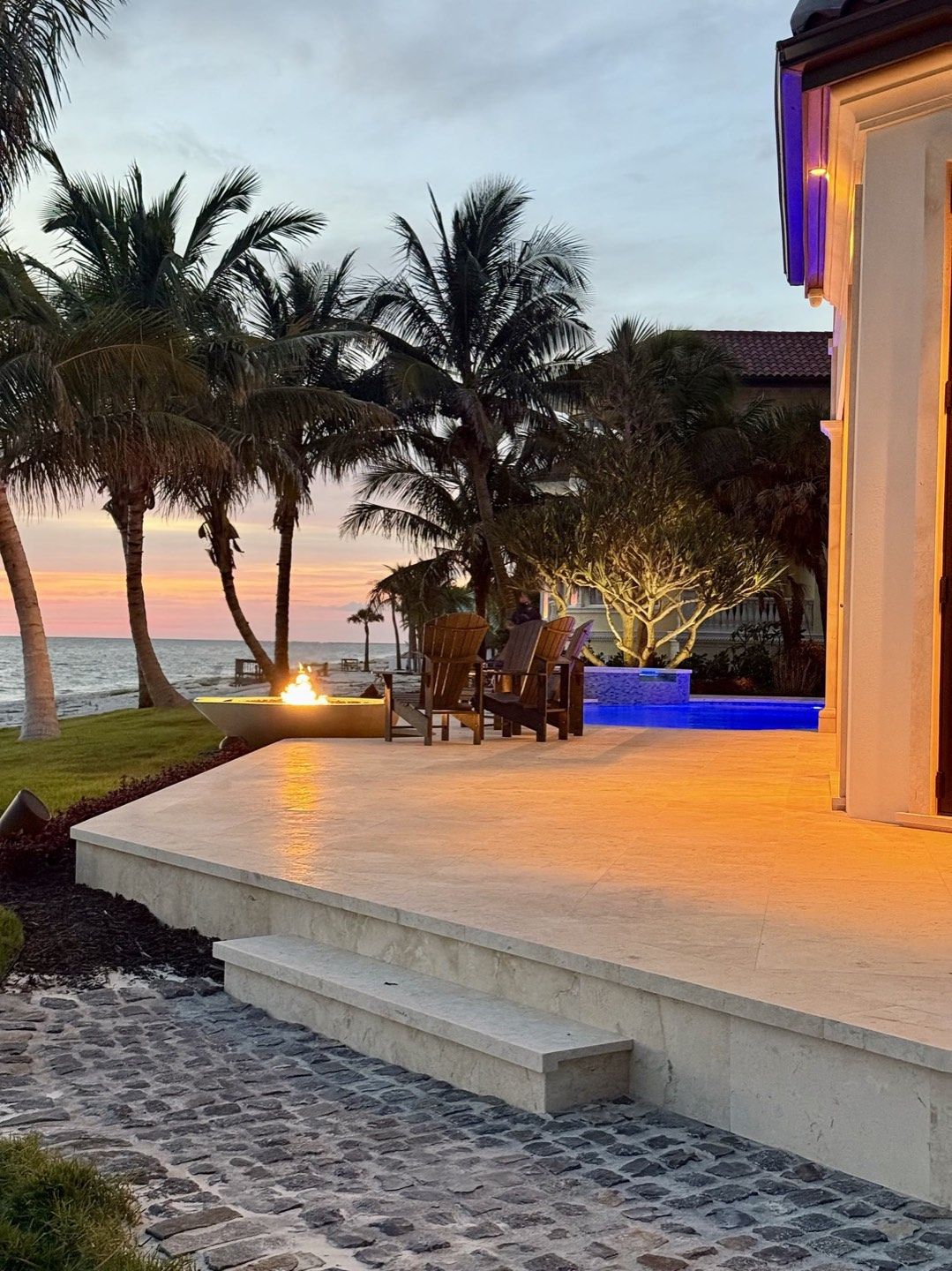 Outdoor living terrace with waterfront seating and a finished firepit setting at dusk