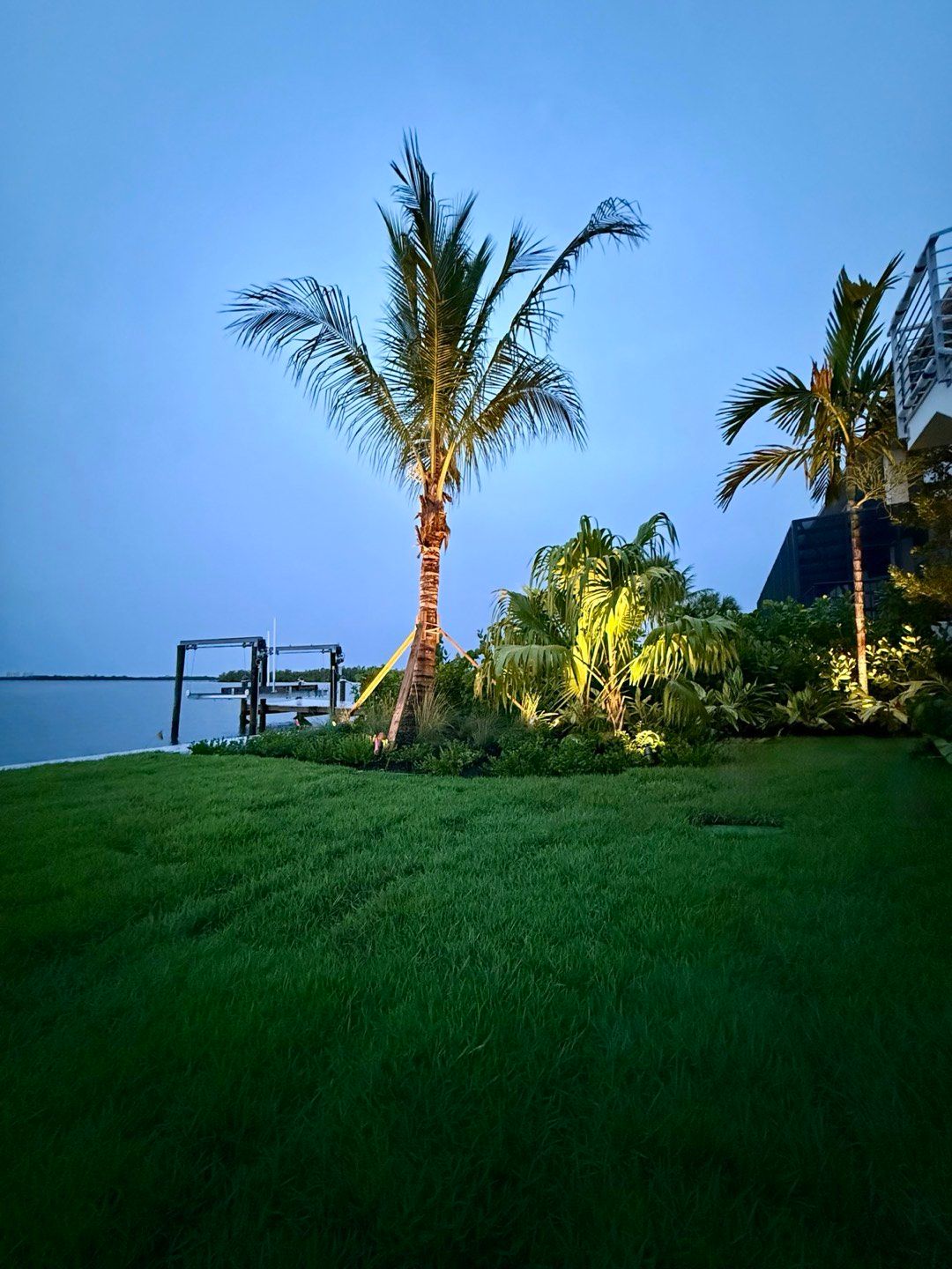 Waterfront planting bed and lawn softly lit at dusk beside a dock